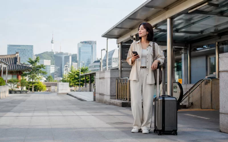 Traveler with suitcase near Seoul station checking phone for luggage storage options