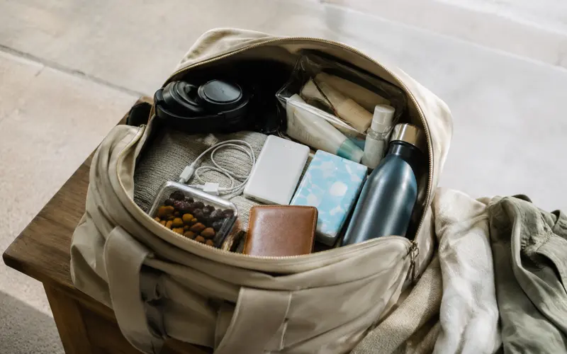 Travel bag packed with headphones, charger, water bottle, toiletries, snacks, and other essentials.