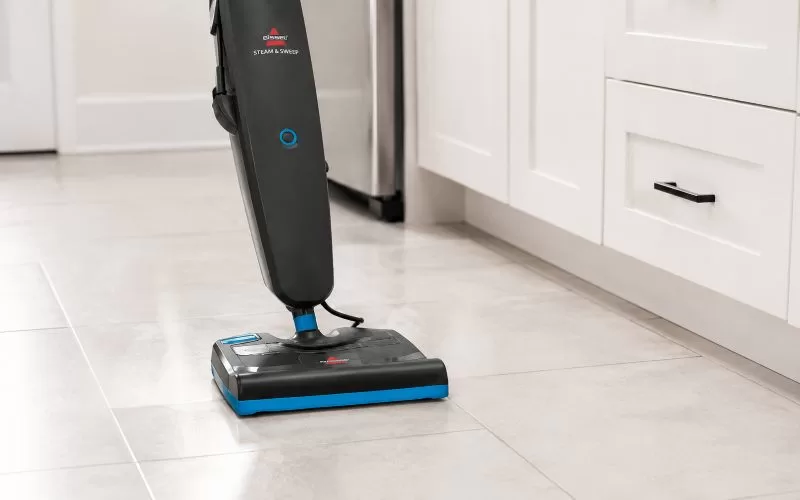 Close-up of the BISSELL Steam & Sweep mop head cleaning light tile flooring in a bright kitchen.