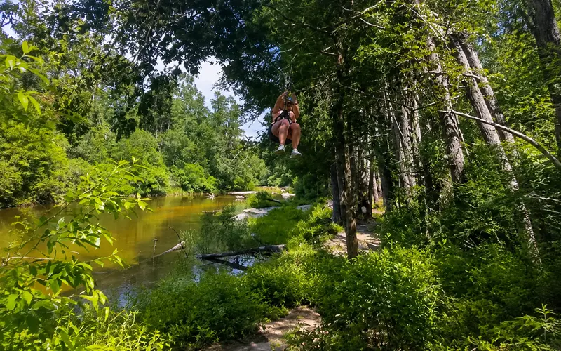 Person ziplining above a wooded creek at Adventures Unlimited in Milton, Florida
