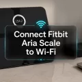 Fitbit Aria scale near a Wi-Fi router with centered text that says Connect Fitbit Aria Scale to Wi-Fi.