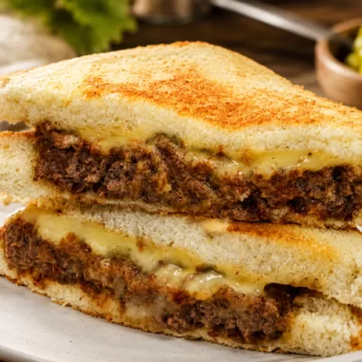 Italian cube steak sandwich with melted cheese on toasted bread served on a plate with a rustic kitchen background