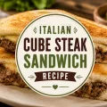 Italian cube steak sandwich with melted cheese on toasted bread featured on a rustic background with title graphic overlay