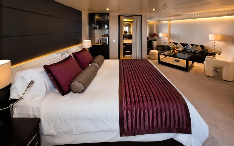 Norwegian Getaway Owner’s Suite with a king-size bed, burgundy accents, and adjoining living area