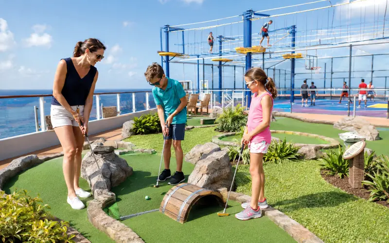 Family playing miniature golf in a cruise ship recreation area during a sunny day at sea.