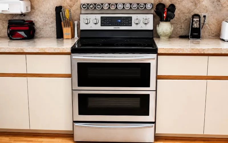Samsung Dual Cook electric range in a kitchen with light cabinets and beige tile backsplash