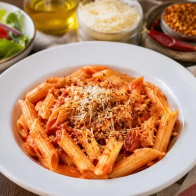 Spicy marinara penne pasta served with garlic bread, green salad, Parmesan cheese, and red pepper flakes.