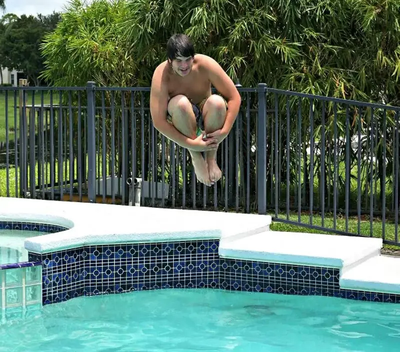 Boy captured in midair doing a cannonball into a backyard swimming pool