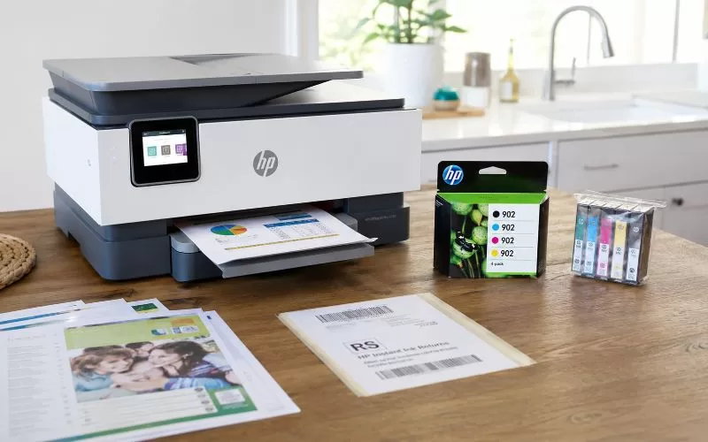 Home printer with unopened replacement ink cartridges, printed documents, and a return label on a clean counter.