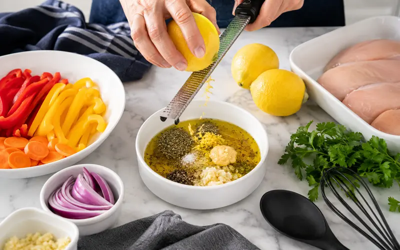 Lemon herb chicken marinade being prepared with fresh lemon, garlic, Dijon mustard, olive oil, and herbs.