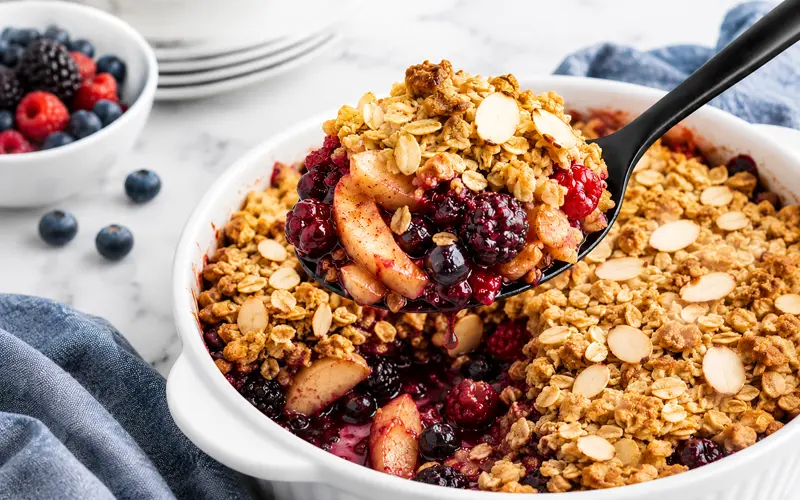 Warm apple berry crumble with a golden oat and almond topping served from a white baking dish