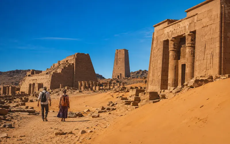 Travelers exploring monumental ancient stone structures in a vast desert landscape.