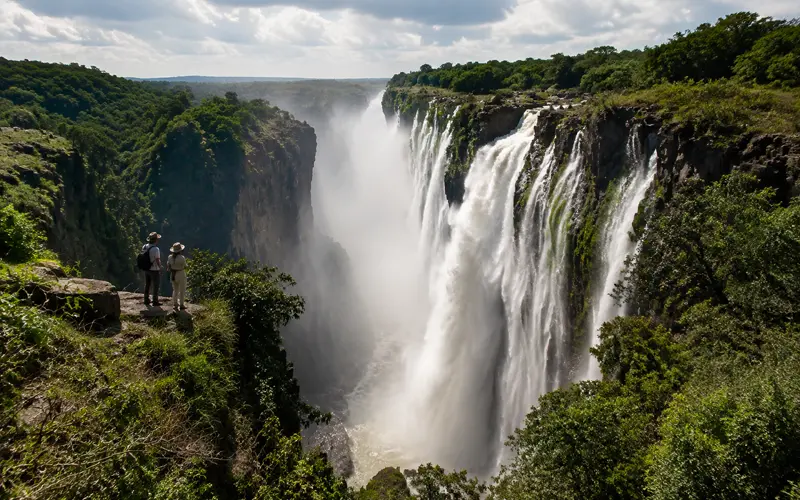 Travelers overlooking a powerful waterfall surrounded by a lush rocky landscape.