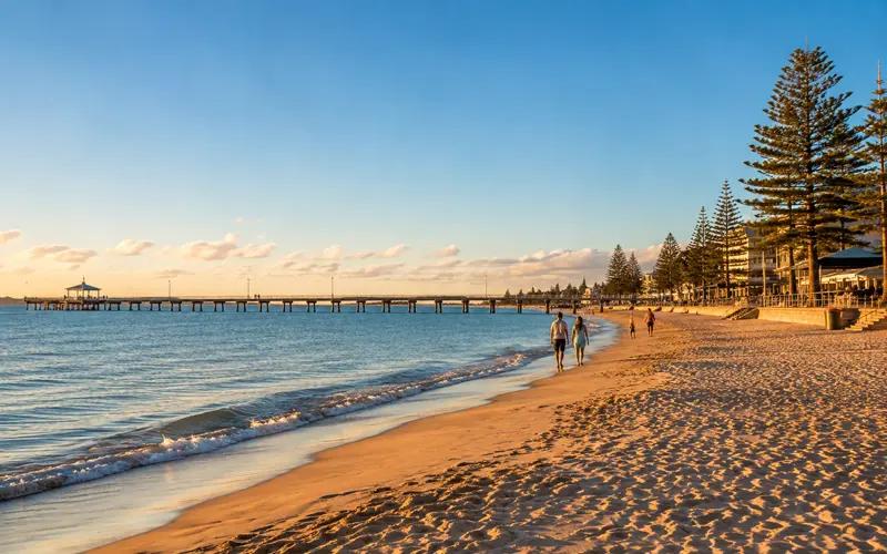 Sandy Australian city beach with calm blue water and a long coastal jetty