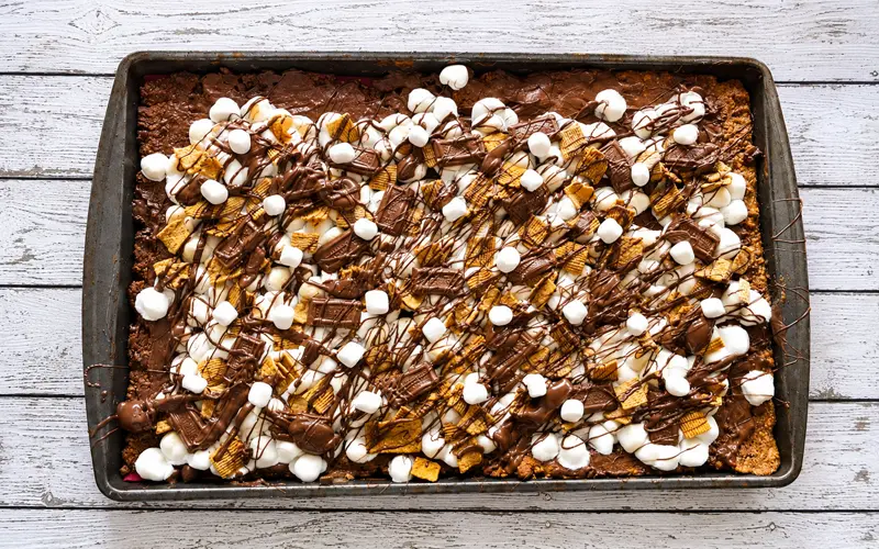 Golden Grahams S’mores Pizza Squares topped with marshmallows, chocolate pieces, cereal, and melted chocolate drizzle.