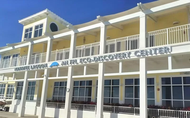 Exterior of Manatee Lagoon Eco-Discovery Center in West Palm Beach with white railings, yellow walls, and a clear blue sky.