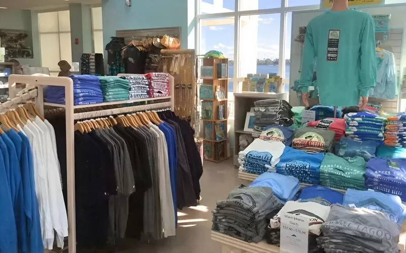 Manatee Lagoon gift shop with folded shirts, clothing racks, souvenirs, and large windows overlooking the water.
