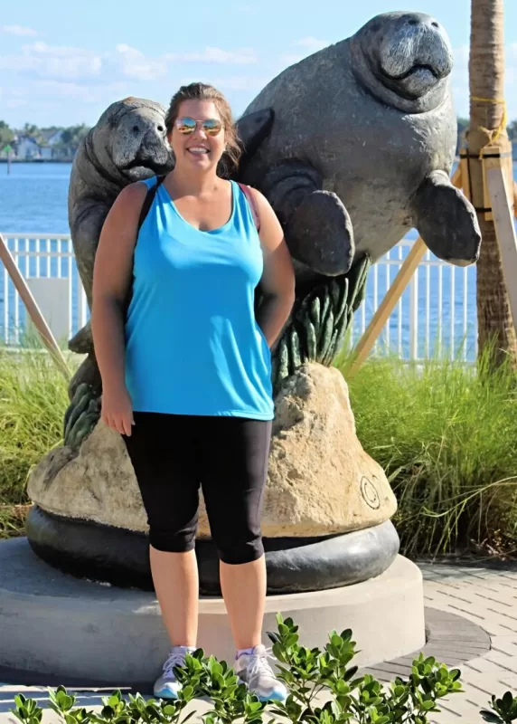 Woman standing beside a manatee statue at Manatee Lagoon in West Palm Beach.