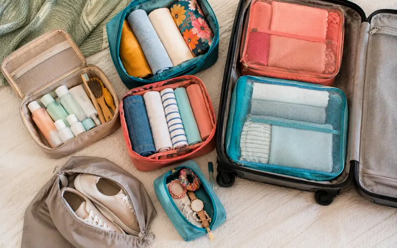 Colorful packing cubes, folded clothing, toiletries, shoes, and travel accessories being organized into a suitcase.