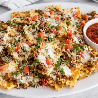 Crispy lasagna nachos topped with Italian sausage, Alfredo sauce, melted mozzarella, Parmesan, diced tomatoes, and basil with marinara for dipping.