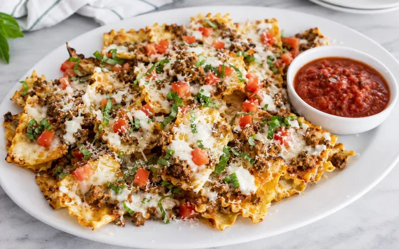 Crispy lasagna nachos topped with Italian sausage, Alfredo sauce, melted mozzarella, Parmesan, diced tomatoes, and basil with marinara for dipping.