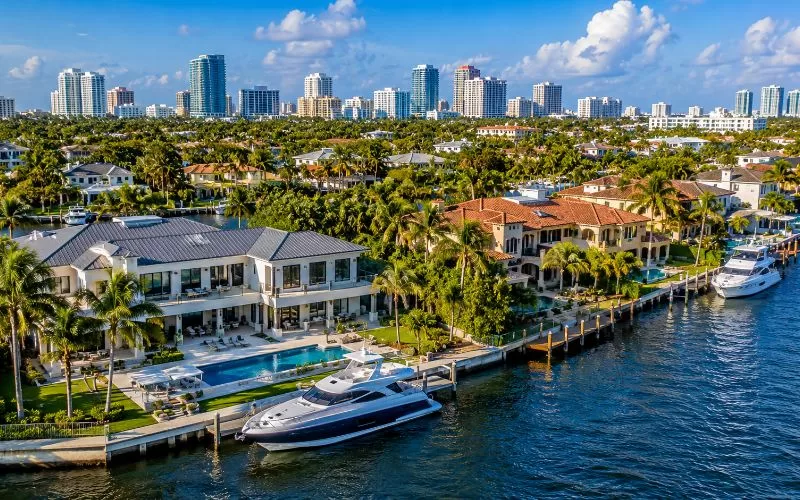Luxury waterfront homes in Fort Lauderdale with private docks, yachts, palm trees, and skyline views from above.