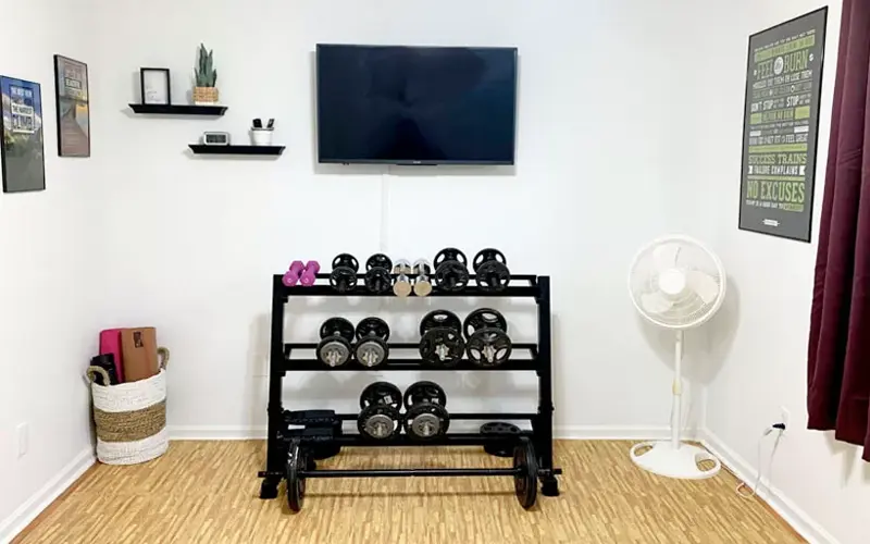 Extra bedroom converted into a home gym with a weight rack, television, foam flooring, fan, and motivational wall art.