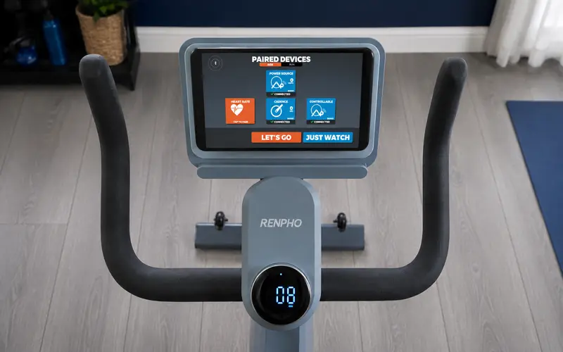 RENPHO AI Smart Bike handlebars and console with paired devices screen in a gray home gym