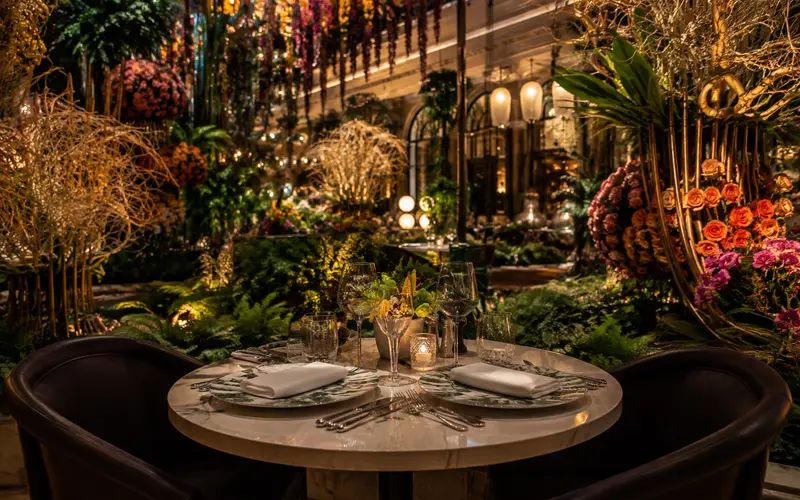 Intimate fine-dining table surrounded by lush flowers and elaborate indoor botanical displays.