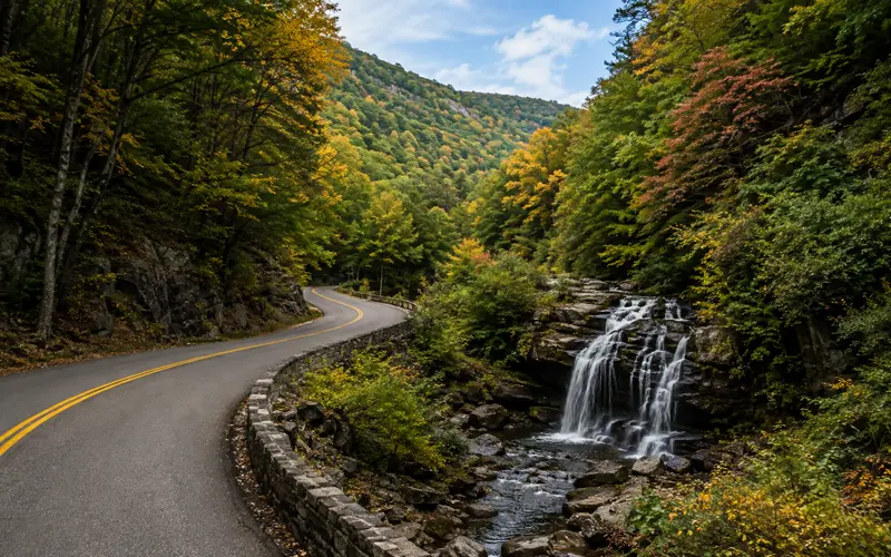 Winding Pennsylvania mountain road beside a natural waterfall surrounded by colorful Appalachian forest.