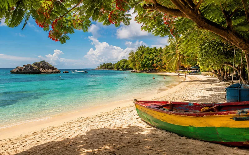 Colorful fishing boat on a turquoise beach in Jamaica beneath tropical trees