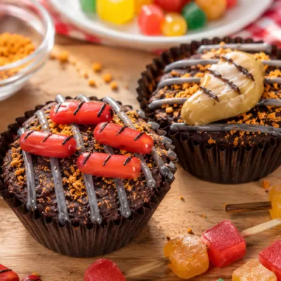 Close-up of two Father’s Day Grillin’ Brownies decorated like mini grills, with candy hot dogs, a candy steak, frosting grill lines, and extra decorating pieces scattered on the table.