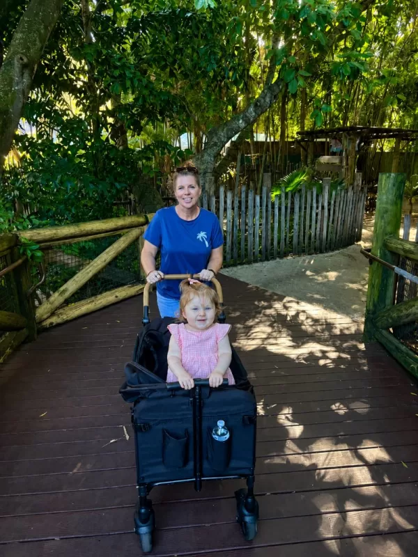 Grandmother pushing a young child in a stroller wagon along a shaded walkway at the Palm Beach Zoo.