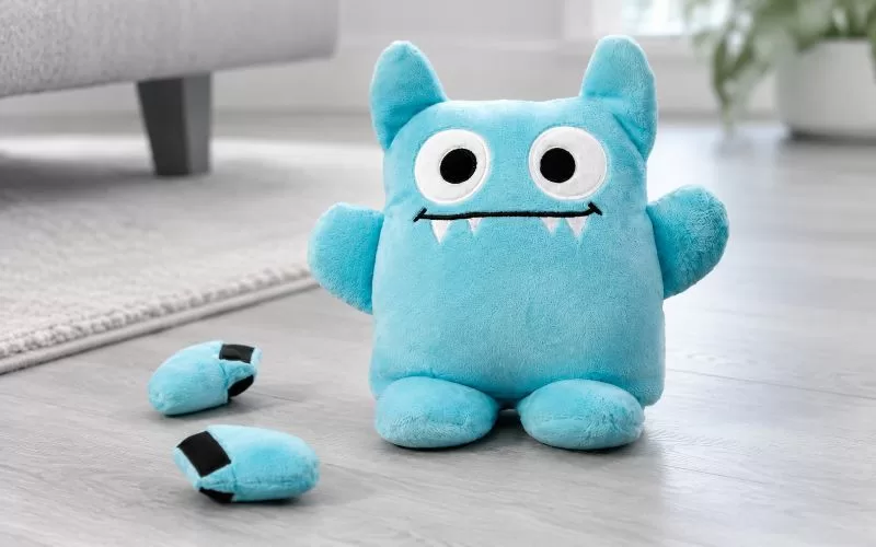 Blue Tearribles plush dog toy sitting on a light gray floor with two detached toy pieces nearby in a bright living room.