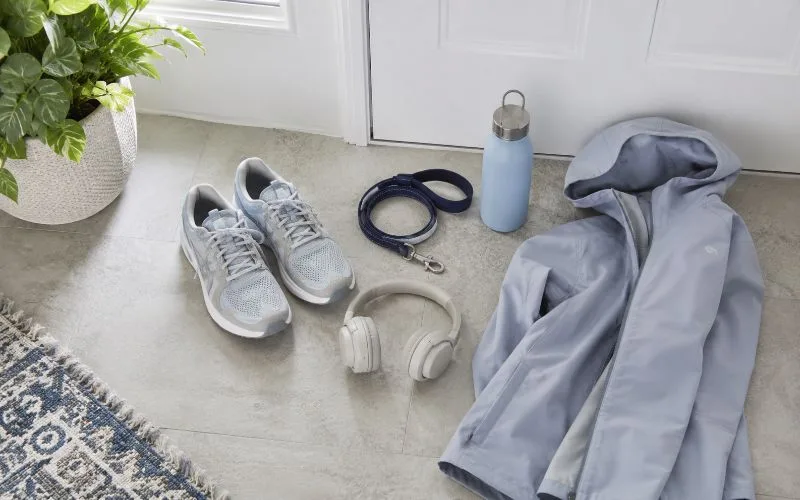 Walking shoes, headphones, dog leash, reusable water bottle, and lightweight jacket arranged near a white front door.