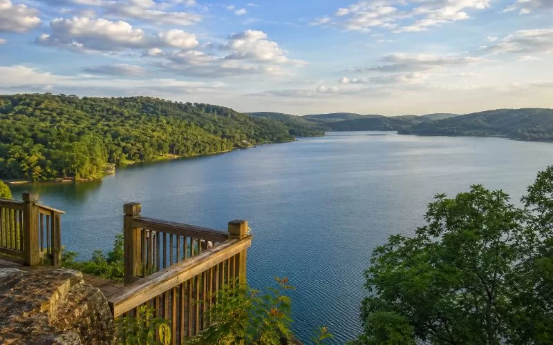 Peaceful Ozarks lake view with calm blue water, tree-covered hills, and a wooden overlook.