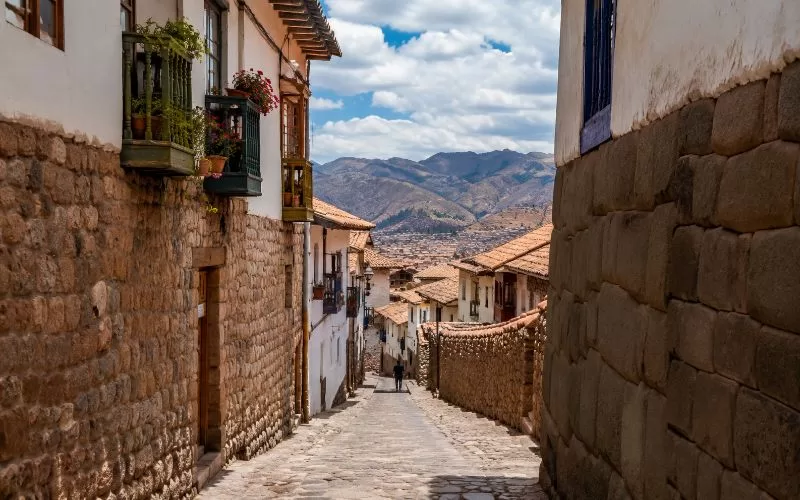Historic Andean street with stone walls, colonial-style balconies, terracotta rooftops, and distant mountain views
