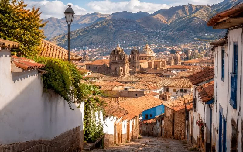 Andean city scene with terracotta rooftops, historic architecture, stone streets, and distant mountains in warm daylight.