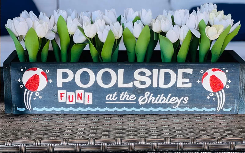 Poolside wooden box filled with white faux tulips and decorated with beach ball designs.