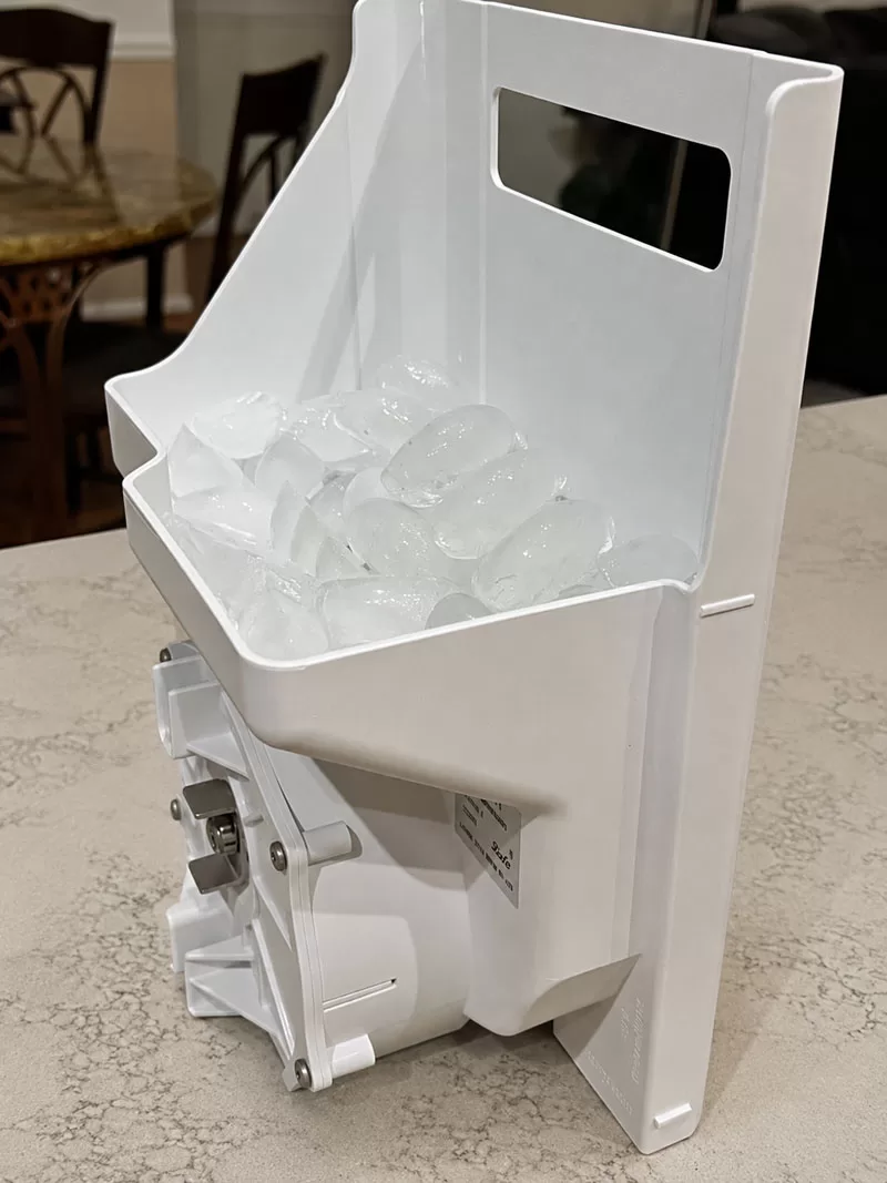 GE refrigerator ice maker bucket filled with ice cubes on granite kitchen countertop