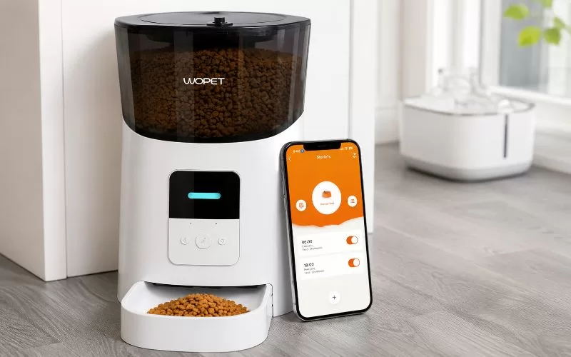 WOPET automatic pet feeder with a smartphone showing scheduled feeding times on the app screen.