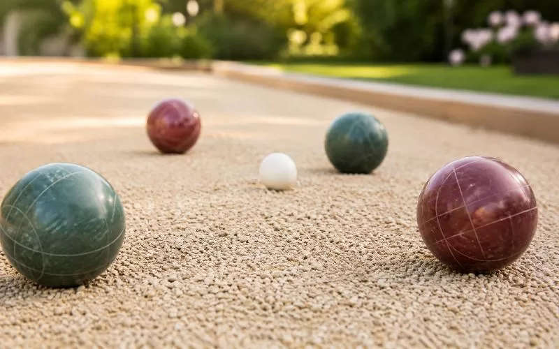Bocce balls on a textured court surface with a small white pallino ball in warm outdoor light.