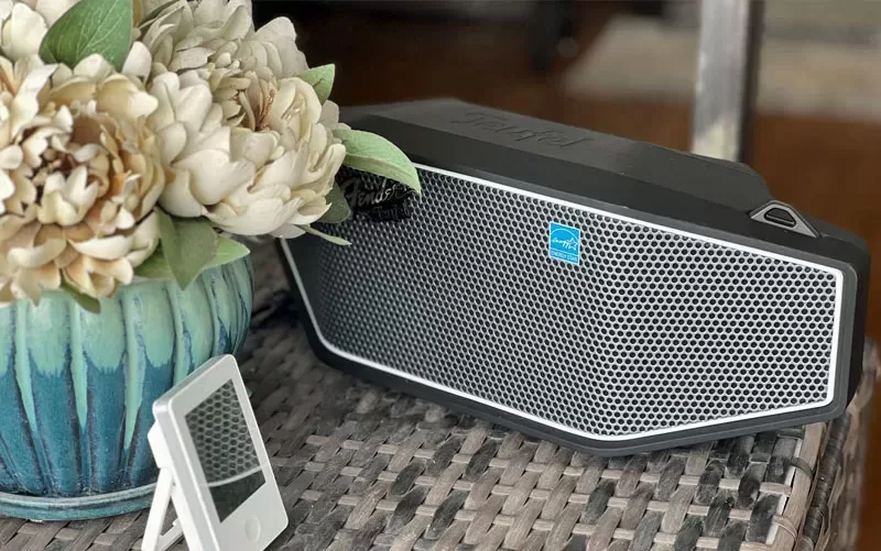 Fender x Teufel ROCKSTER CROSS Bluetooth speaker on an outdoor patio table beside a flower arrangement
