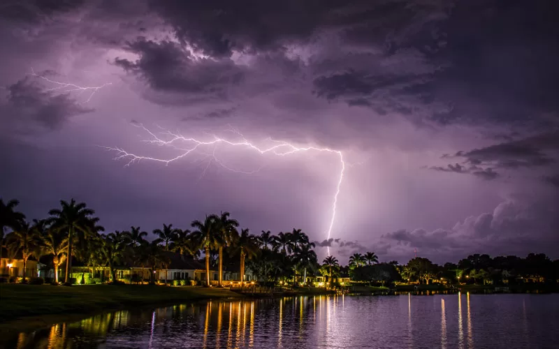 Dramatic Florida thunderstorm with lightning striking over a lake lined with palm trees and waterfront homes at night