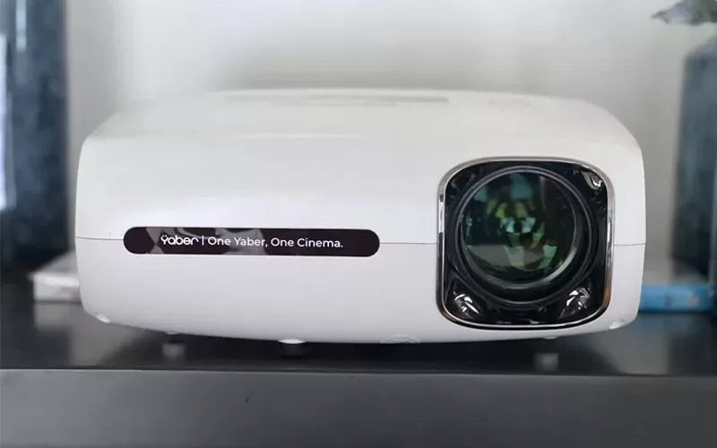 White projector sitting on a shelf for a holiday window projection setup