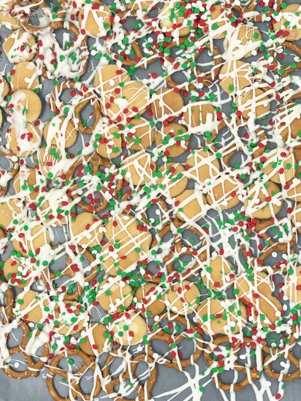 Close-up of vanilla wafer cookies and pretzels drizzled with white chocolate and topped with red, green, and white holiday sprinkles for Festive Sweet Maple Christmas Chex Mix.