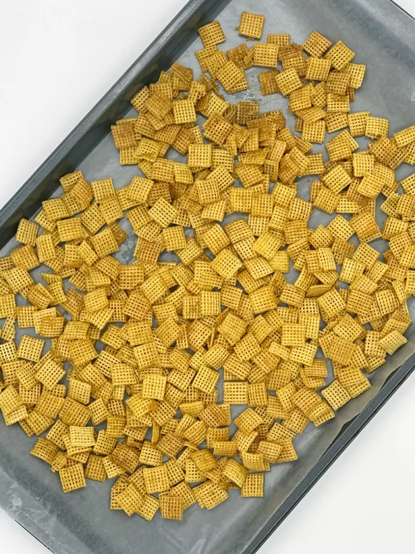 Maple-coated Chex cereal spread across a parchment-lined baking sheet while cooling for Festive Sweet Maple Christmas Chex Mix.