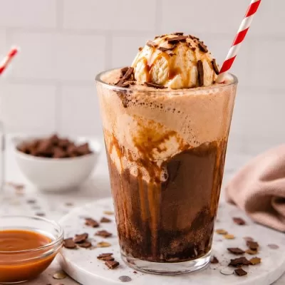 Salted caramel brownie float topped with vanilla ice cream, caramel drizzle, and chocolate shavings in a tall glass with striped straw.