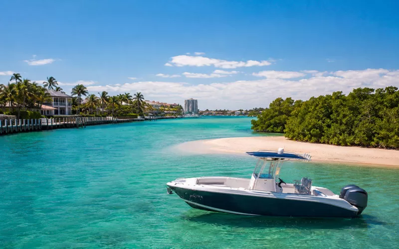 Florida waterway with a boat near a sandy shoreline, mangroves, and clear blue-green water under a sunny sky.