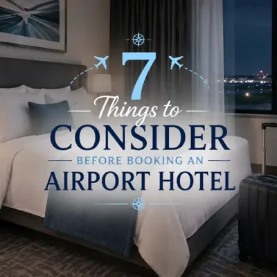 Modern hotel room with a made bed, rolling suitcase, charging phone, and airport runway lights outside the window.